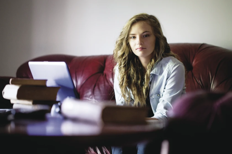 Amanda seated on a red couch beside a laptop and books